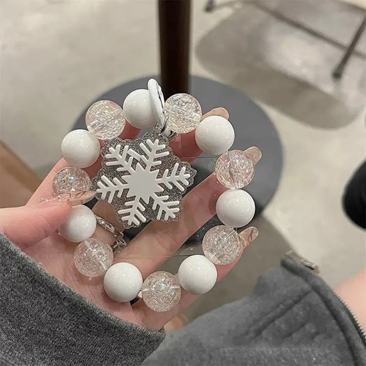 Hand holding a decorative keychain with snowflake design and white and glittery beads.