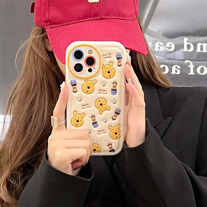 Person holding a phone with a Winnie the Pooh-themed case, wearing a red cap and black coat.