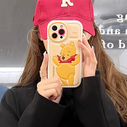 Person holding a phone case with a cartoon bear design, wearing a red cap and black jacket.