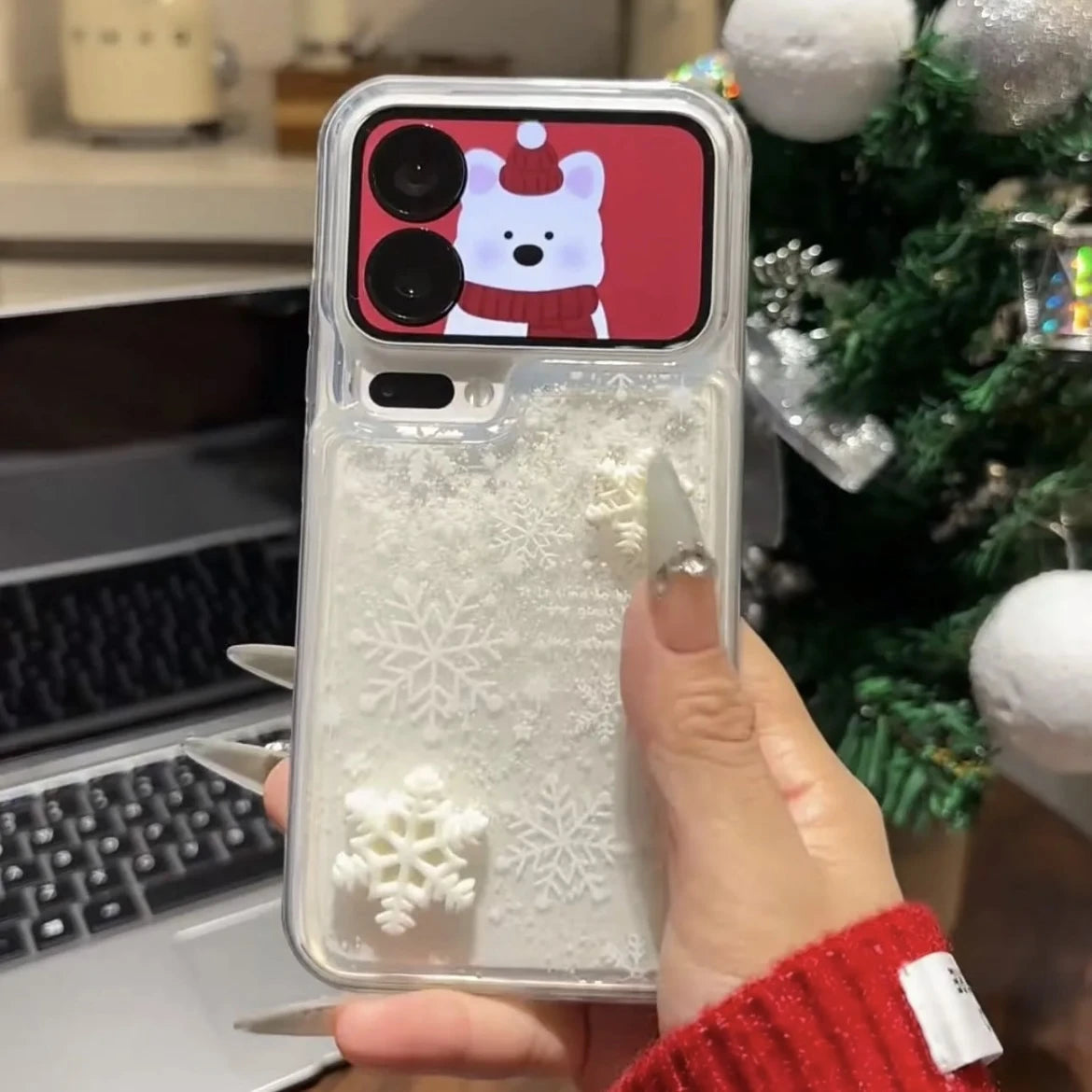 Phone case with Christmas design held by a person in front of a decorated Christmas tree.