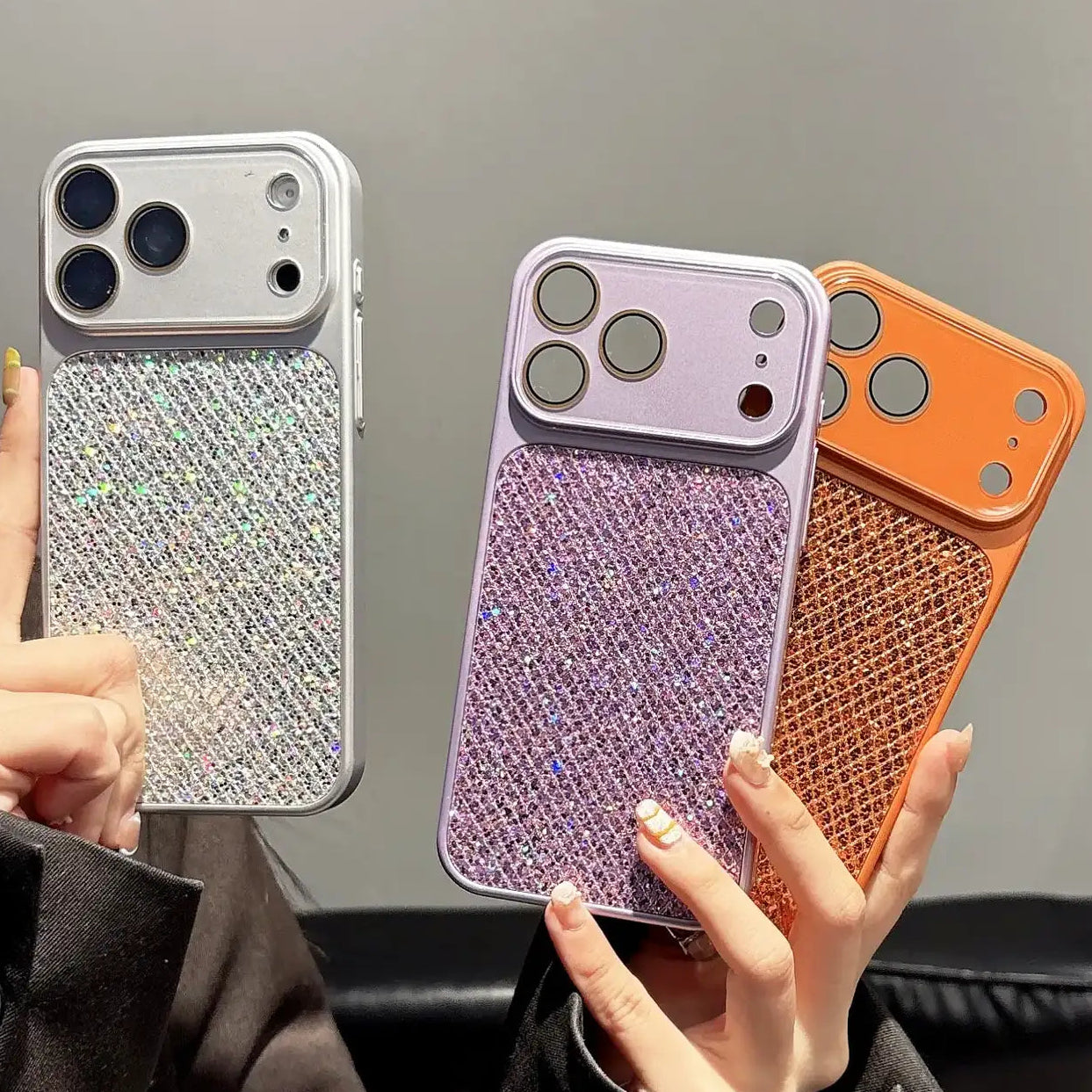 Three phone cases in silver, purple, and orange held by a person against a neutral background.