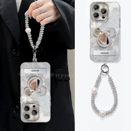 Silver phone case with decorative elements and metal bracelet held by a person wearing a black suit.